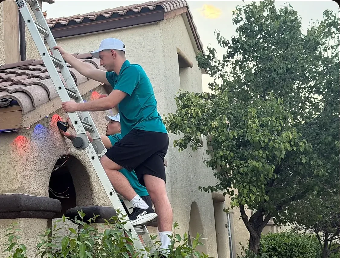 A Magic Season Lighting installer on a ladder fixing lights under a tile roof