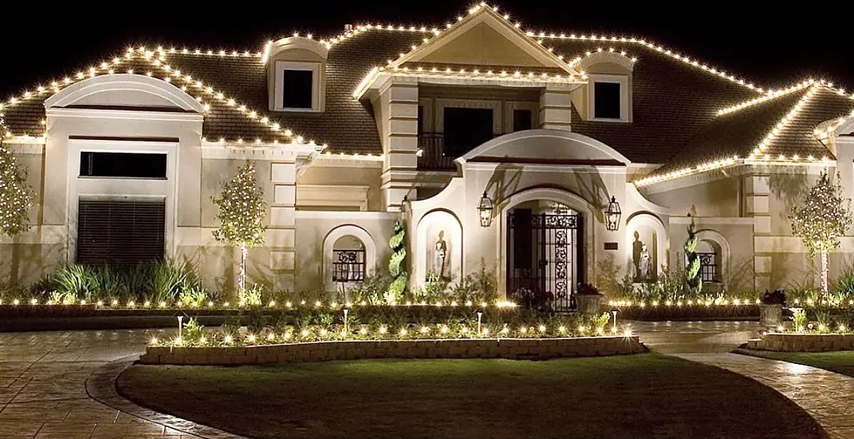 Large stucco estate outlined in warm white roofline lights with lit pathway