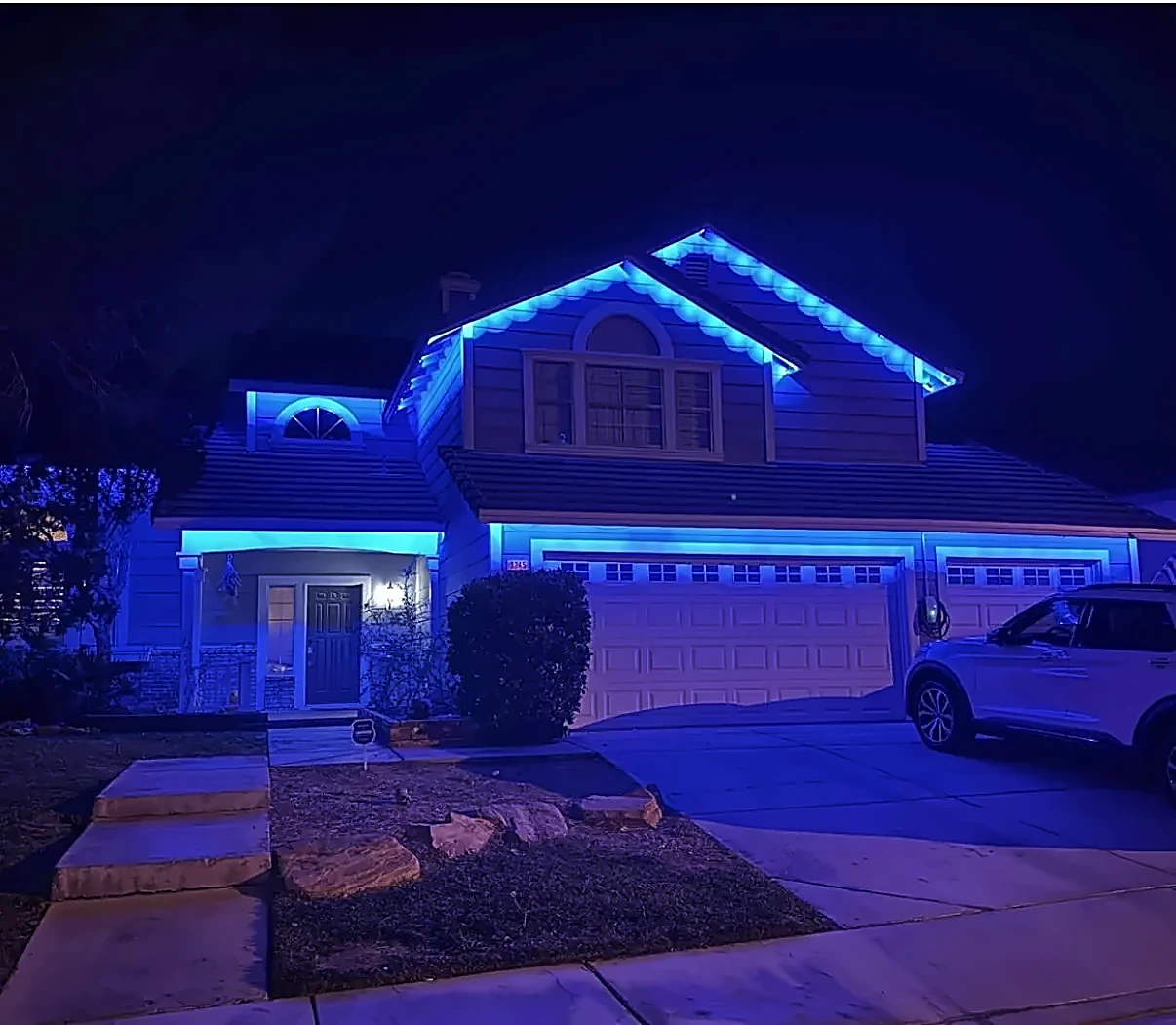 Two-story home with permanent roofline lights set to blue in a scalloped pattern
