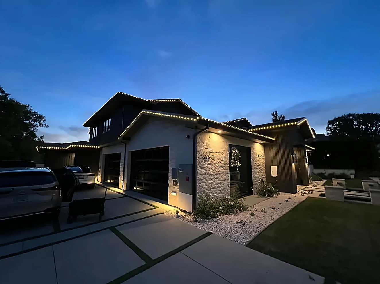 Modern two-story home with warm white lights along every roofline at dusk