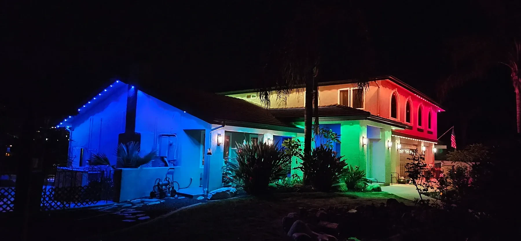 Two-story home washed in blue, green and red from its roofline lights